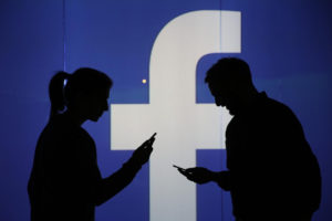People are seen as silhouettes as they check mobile devices whilst standing against an illuminated wall bearing Facebook Inc.s logo in this arranged photograph in London, U.K., on Wednesday, Dec. 23, 2015. Facebook Inc.s WhatsApp messaging service, with more than 100 million local users, is the most-used app in Brazil, according to an Ibope poll published on Dec. 15. Photographer: Chris Ratcliffe/Bloomberg via Getty Images